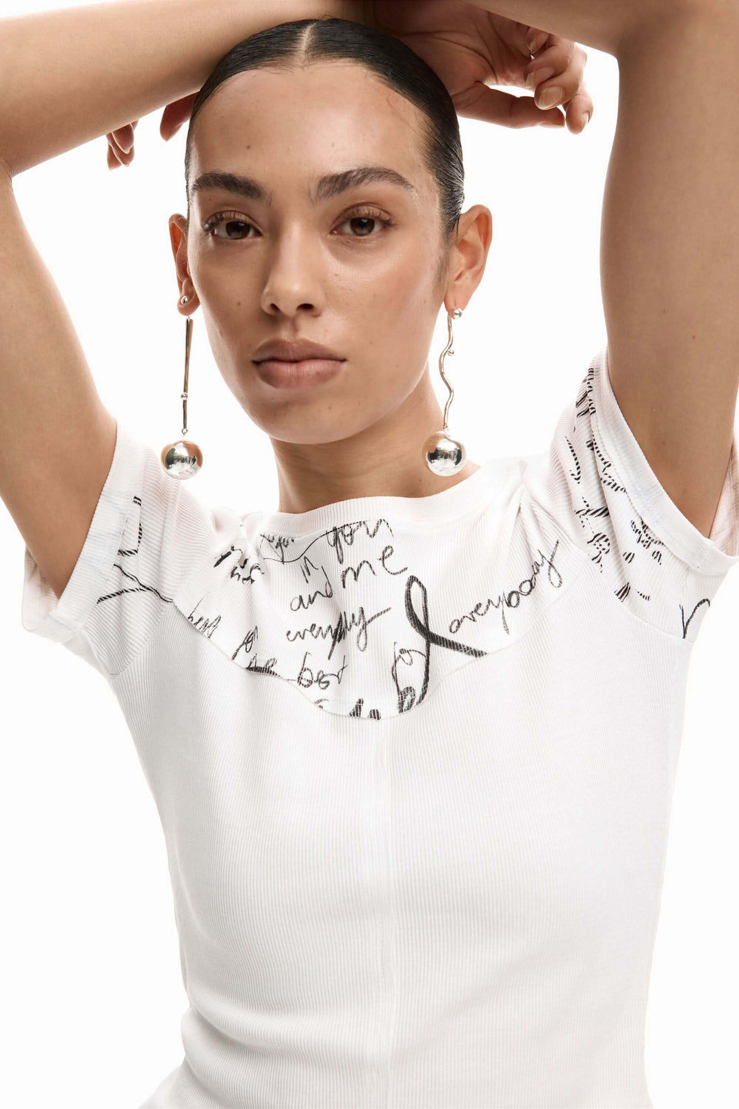 Femme portant un t-shirt ajusté avec lettrage graphique et boucles d'oreilles pendantes, style moderne et élégant.