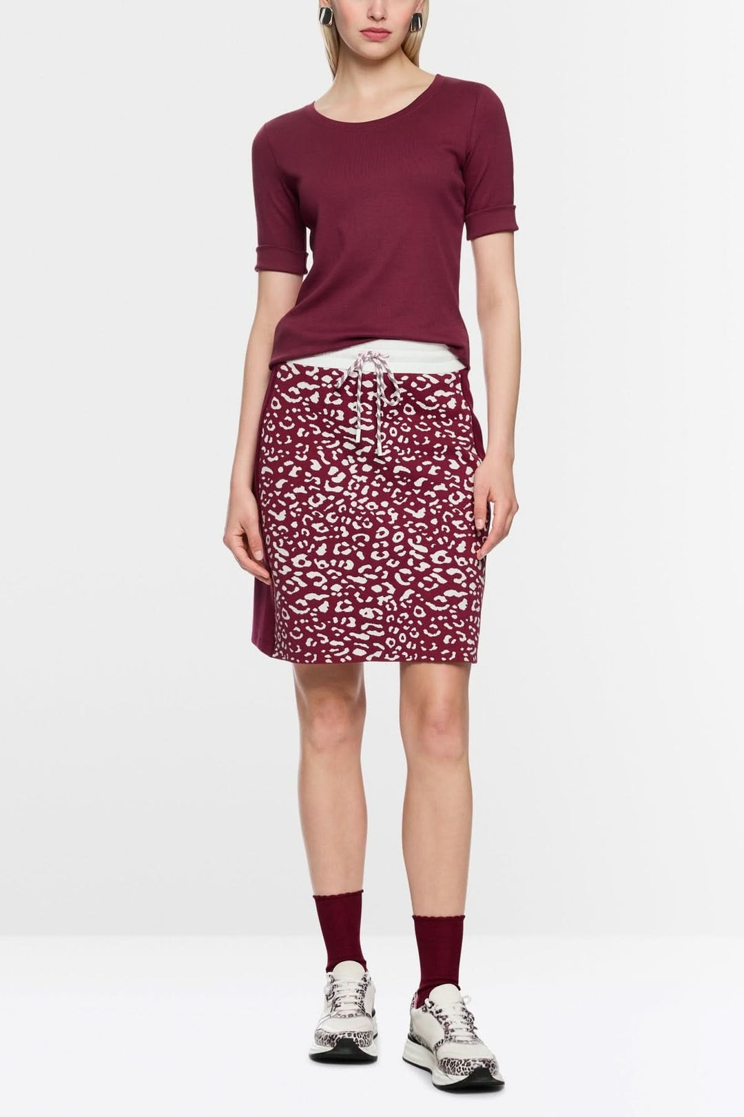 Femme portant un T-shirt ajusté en coton stretch bordeaux avec jupe imprimée, look décontracté.