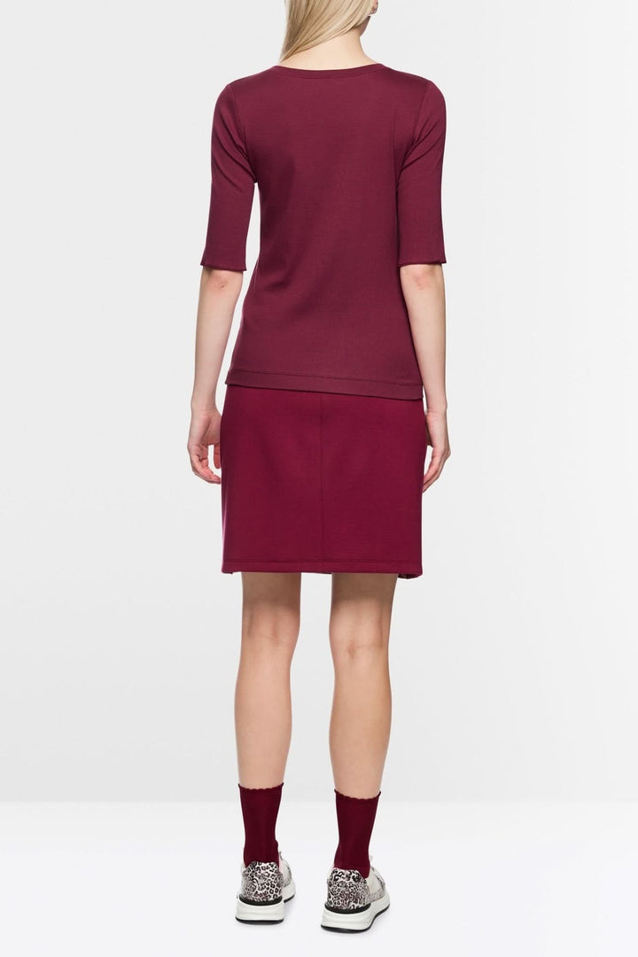 Vue arrière d'un T-shirt ajusté en coton stretch bordeaux, manches mi-longues, porté avec une jupe assortie, pour un style décontracté.