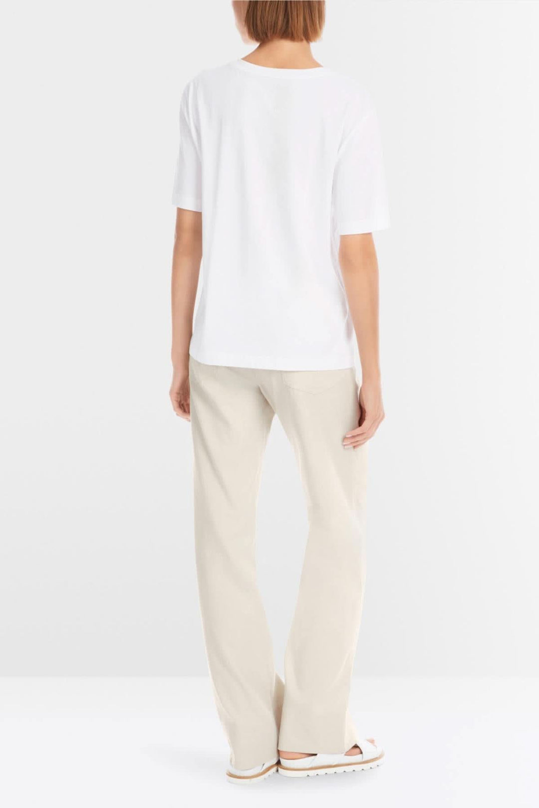 Vue arrière d'un t-shirt blanc décontracté porté avec un pantalon beige, parfait pour une journée d'été.