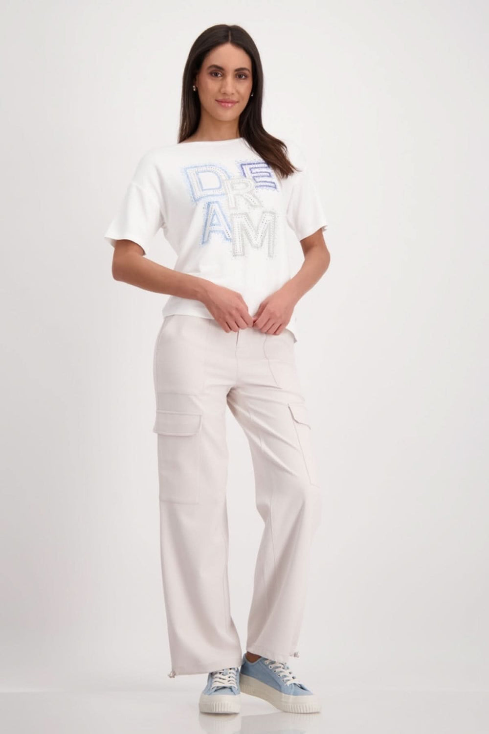 Femme portant un t-shirt blanc avec lettrage "Dream" en strass et un pantalon cargo beige.