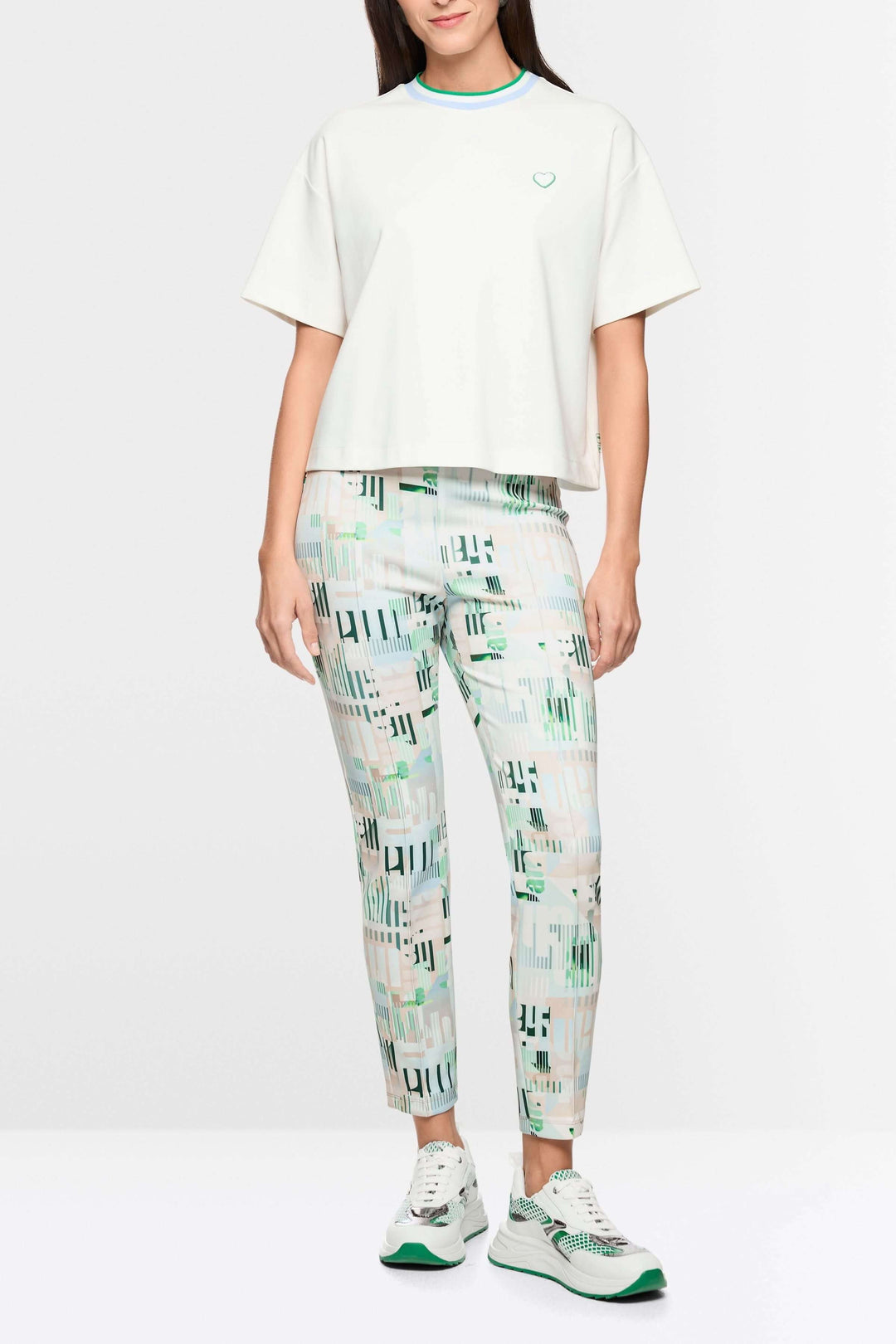 Femme portant un T-shirt avec détails en forme de cœur et à rayures, coupe ample, col contrastant, tenue décontractée avec pantalon imprimé.