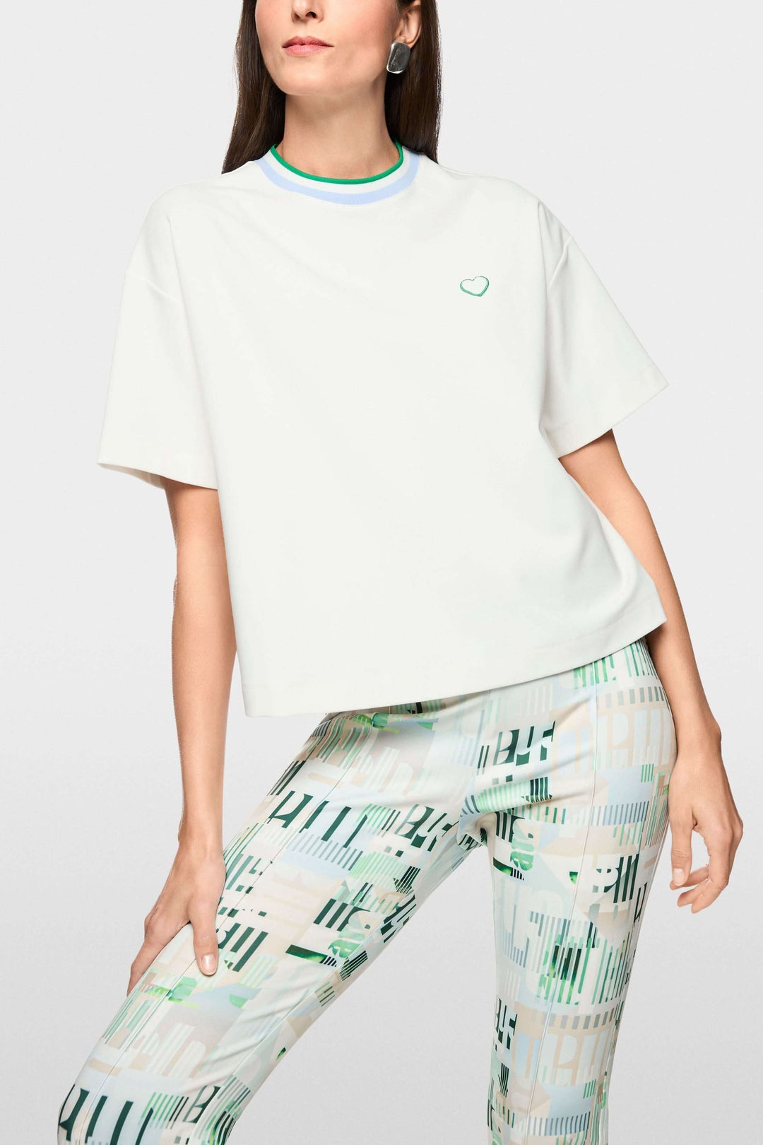 Femme portant un T-shirt avec détails en forme de cœur et à rayures, coupe ample, col contrastant, allure moderne et minimaliste.