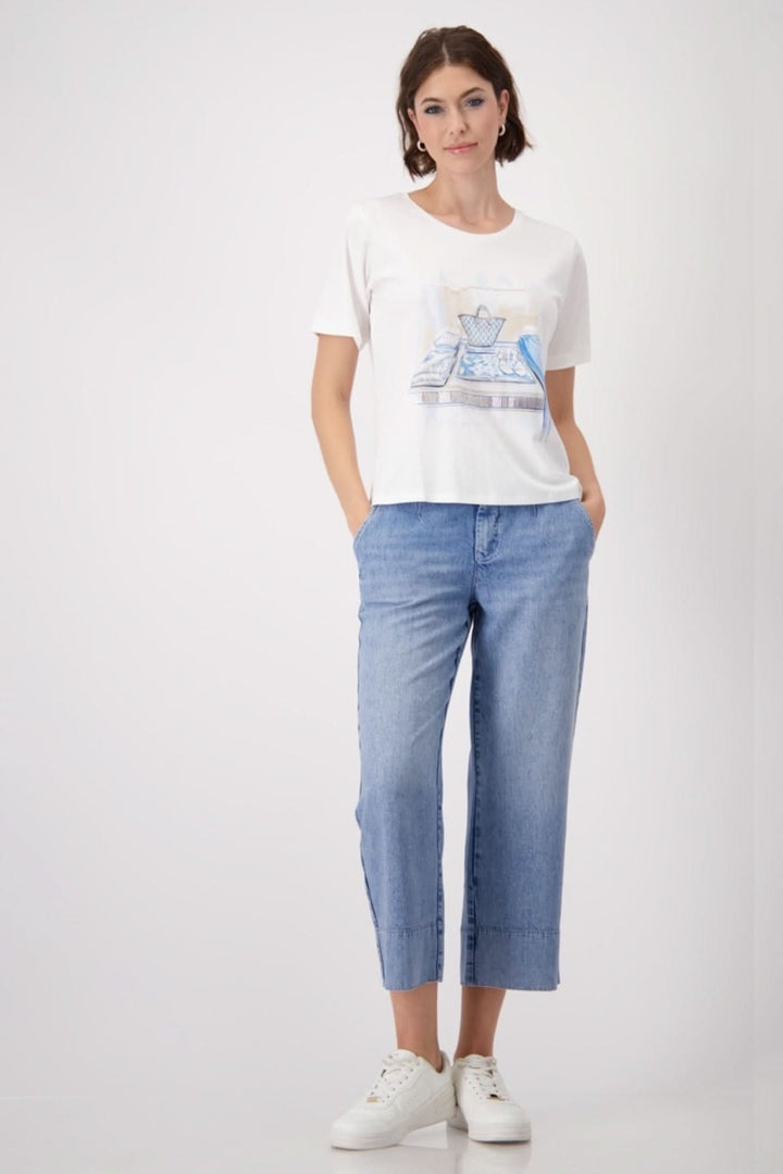 Femme portant un T-shirt blanc à imprimé élégant, associé à un jean clair et des baskets blanches pour un look chic.