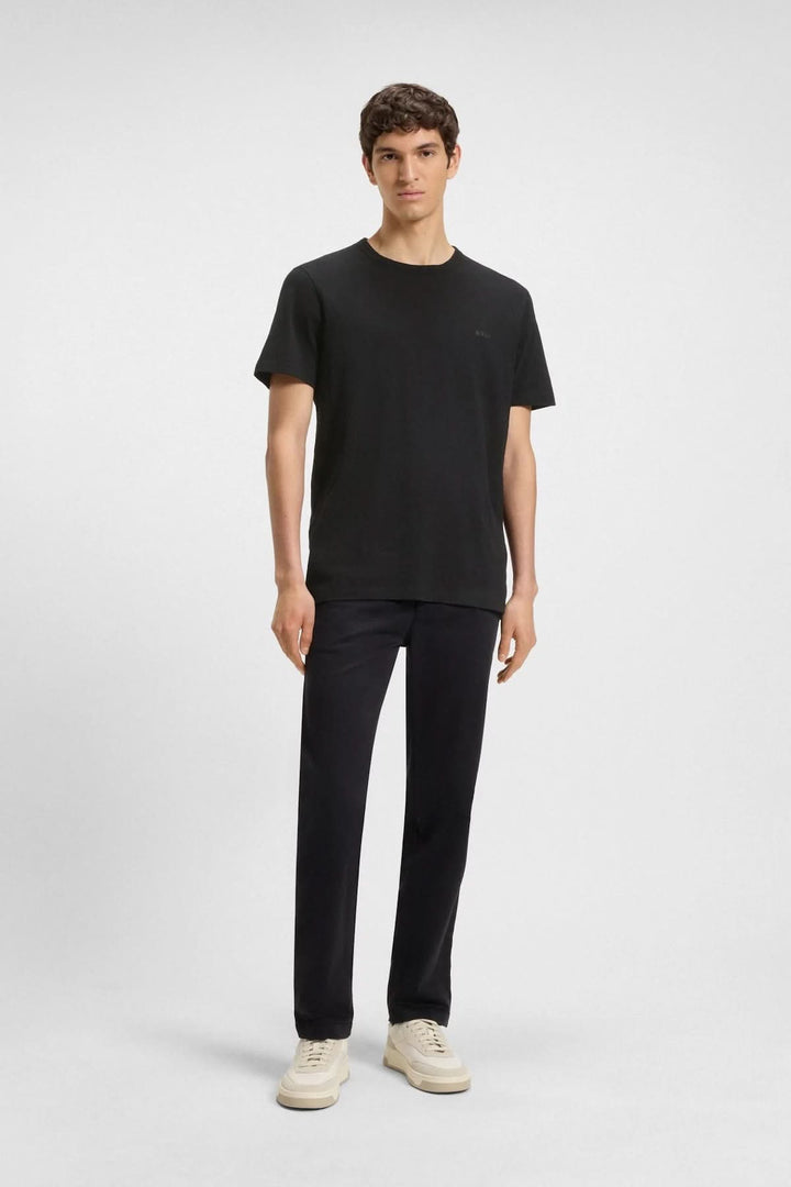 Homme portant un t-shirt noir Boss avec logo brodé, jeans noirs et baskets claires.