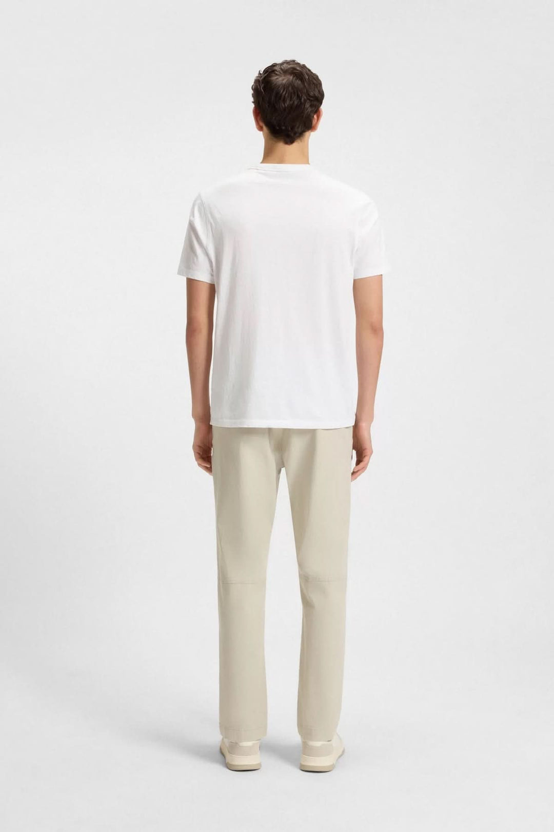 Homme portant un t-shirt blanc dans une coupe droite, vu de dos, avec un pantalon beige.