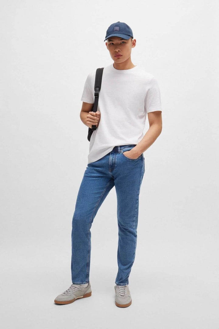 Homme portant un t-shirt blanc, jean bleu, et casquette, avec un sac à dos à l'épaule.