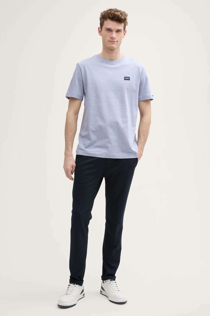 Homme portant un t-shirt minimaliste en coton avec un logo, associé à un pantalon foncé pour un look décontracté.