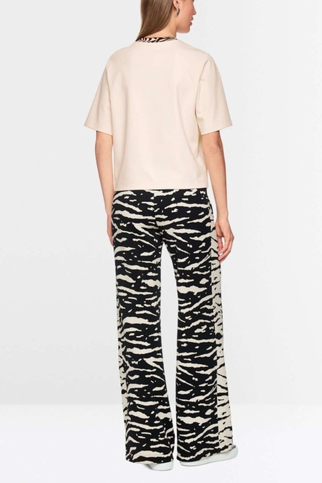 Vue arrière d'un mannequin portant un T-shirt classique Marc Cain Sport beige avec col contrasté et pantalon à motif.