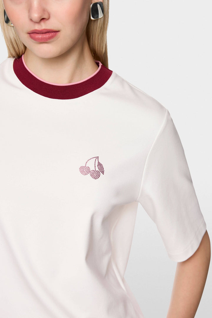 Femme portant un t-shirt classique avec col contrasté et logo cerise discret, manches courtes, en coton doux.
