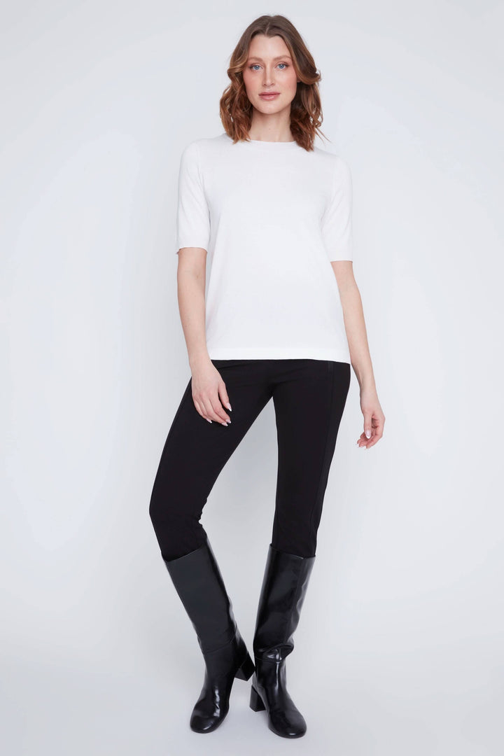 Femme portant un t-shirt classique blanc avec un pantalon noir et des bottes, style minimaliste et élégant.