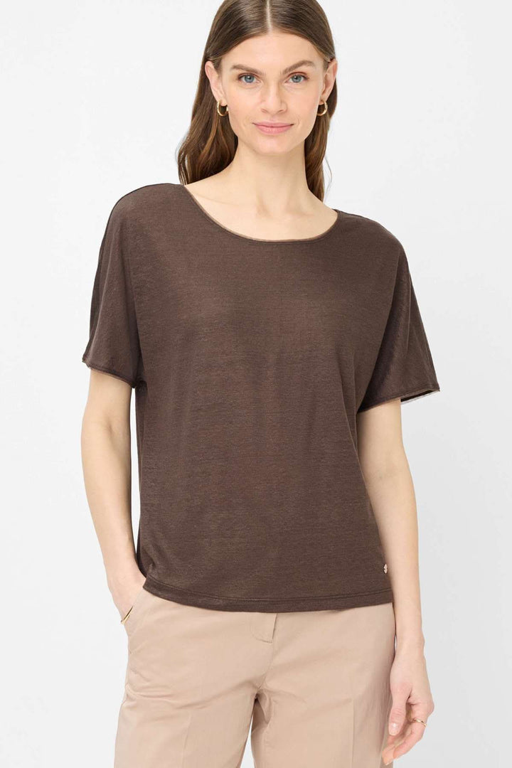 Femme portant un T-shirt col bateau Caelen brun à manches courtes, coupe fluide, avec un pantalon beige, look décontracté mais soigné.