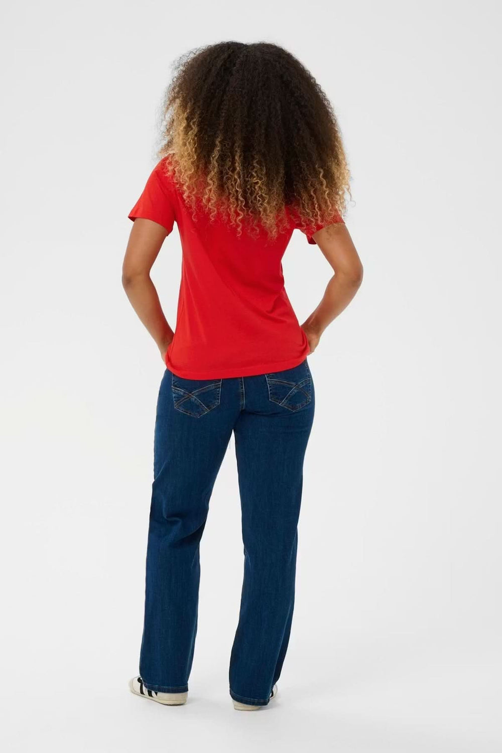 Vue arrière d'une femme portant un T-shirt col en V rouge, mis en valeur avec un jean décontracté.