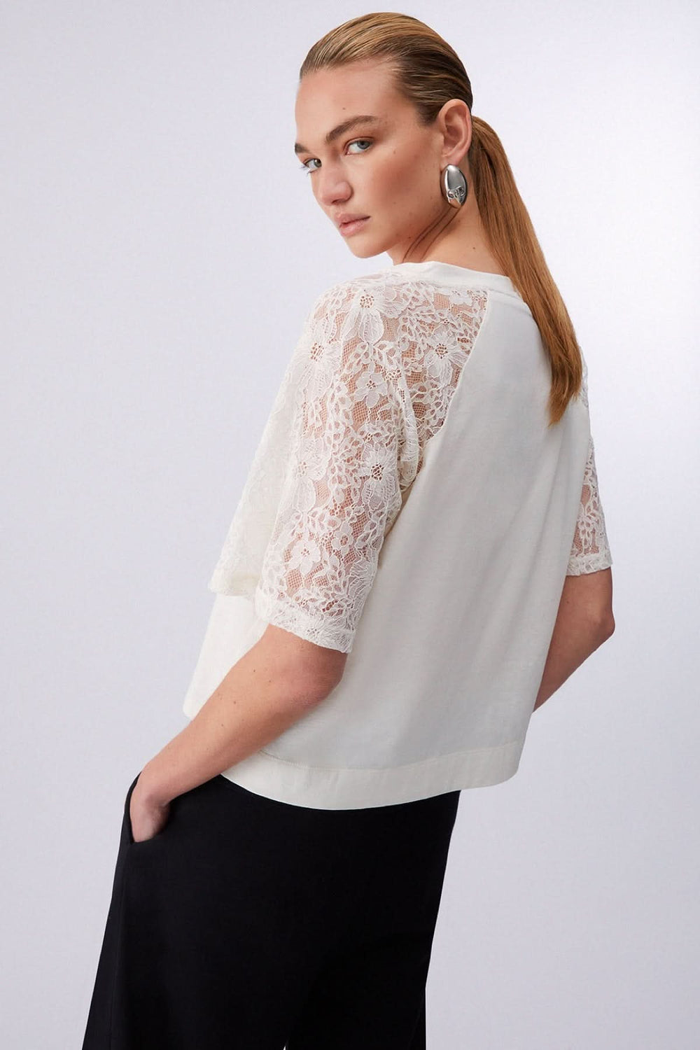 T-shirt à col en V avec manches en dentelle vécu par une femme, offrant une élégance raffinée et un look confortable.