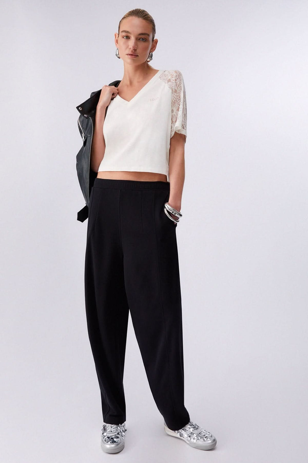 Femme portant un t-shirt à col en V avec manches en dentelle, associé à un pantalon noir, style élégant et moderne.