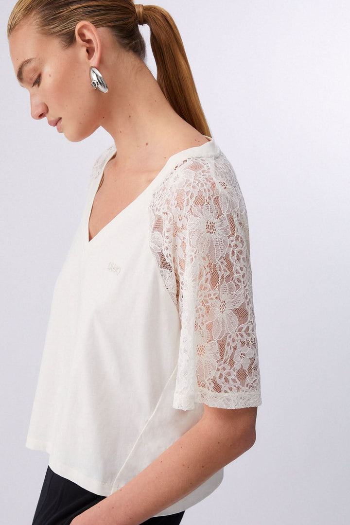 Femme portant un t-shirt à col en V avec manches en dentelle, offrant une silhouette élégante et féminine.