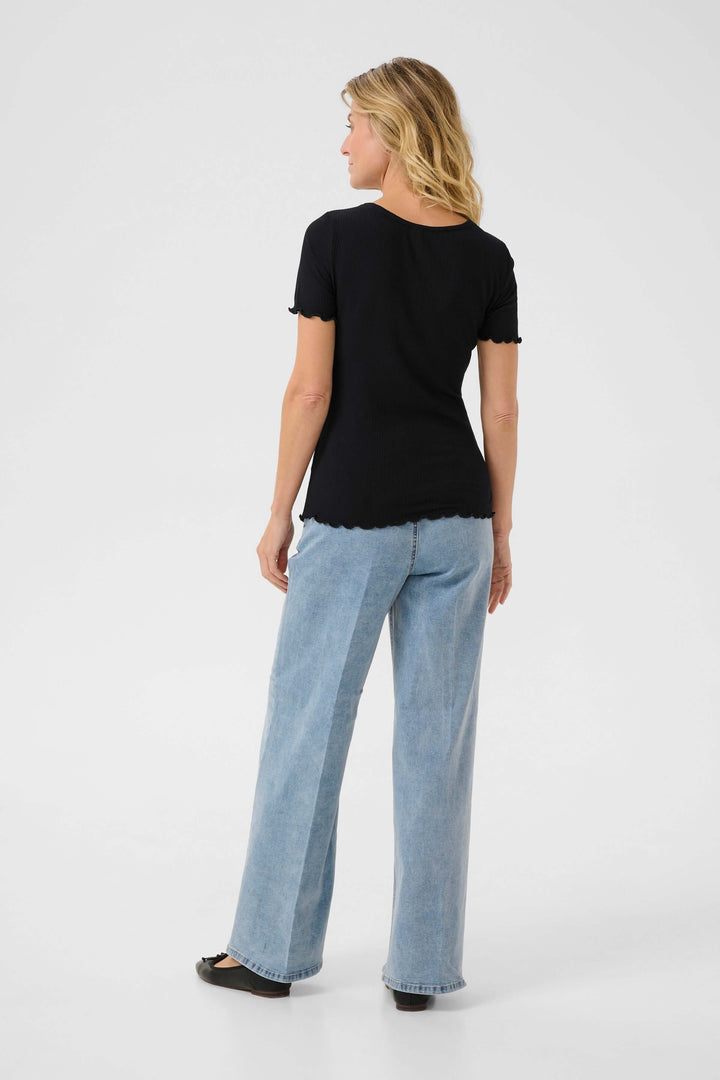 Femme portant un t-shirt noir à col rond et un pantalon bleu clair, vue arrière.