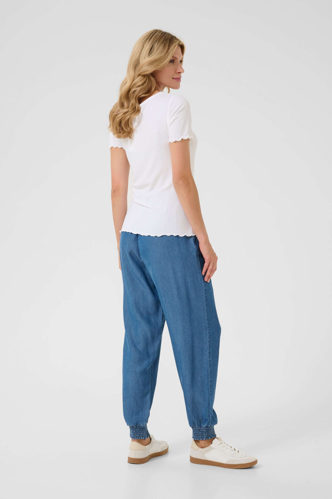 Femme vue de dos portant un t-shirt blanc à col froncé et un pantalon bleu décontracté, style décontracté et élégant.