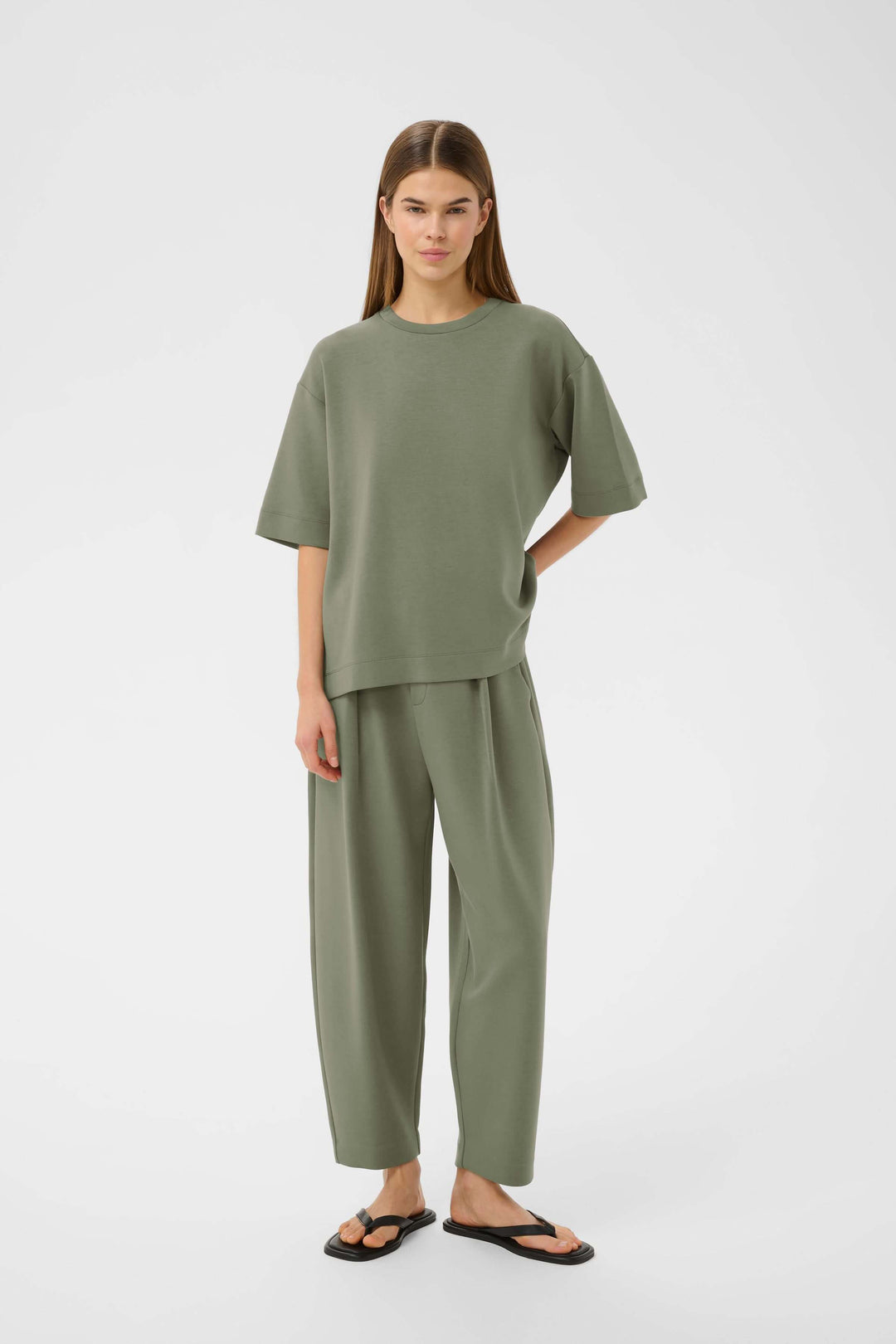 Femme portant un T-shirt Pannie ample et fluide, style décontracté vert avec un pantalon coordonné, manches courtes et encolure ronde.
