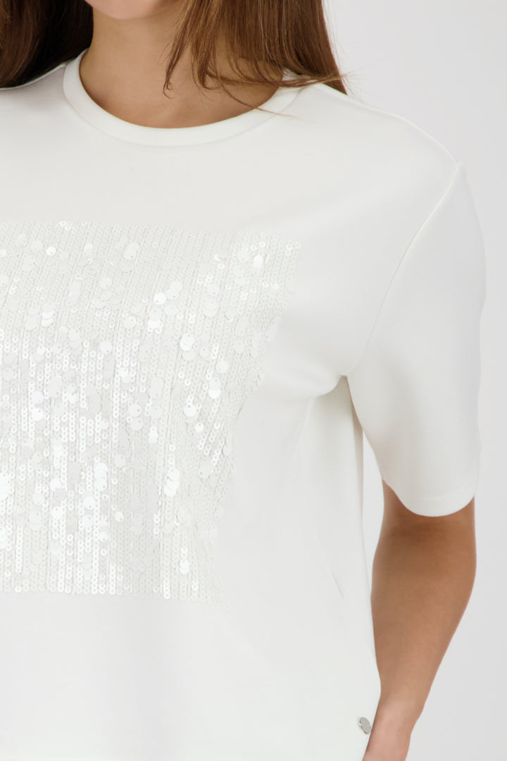 Femme portant un T-shirt à empiècement pailleté avec encolure ronde et manches courtes, ajoutant éclat à un look moderne.