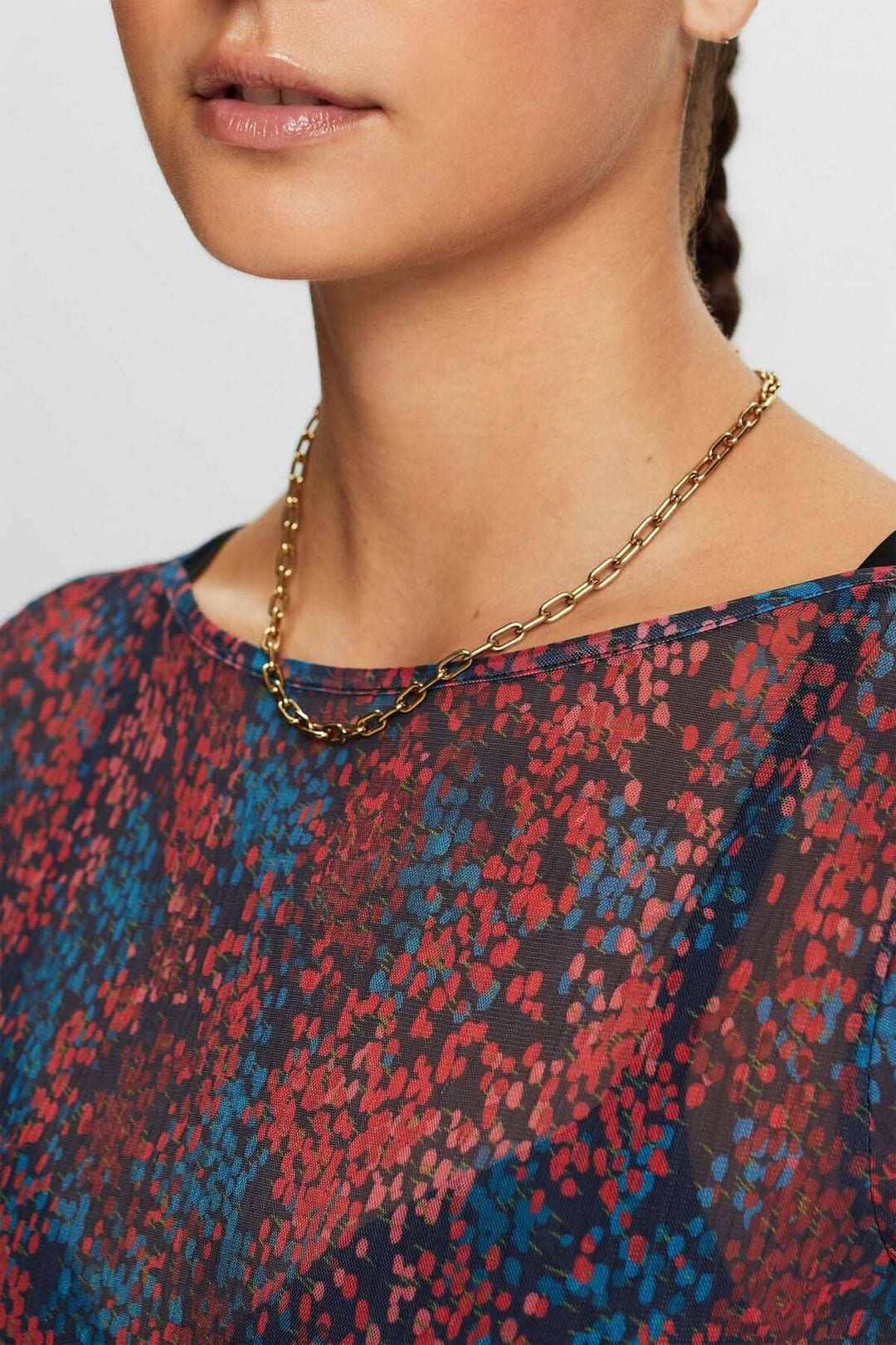 Haut en mesh plissé à motifs colorés, avec décolleté dégagé et collier en chaîne doré.