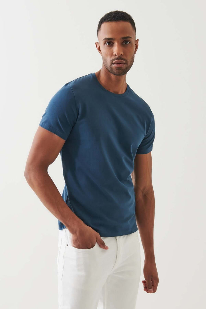 Homme portant un T-shirt en coton Pima bleu avec un style décontracté et élégant, associé à un pantalon blanc.