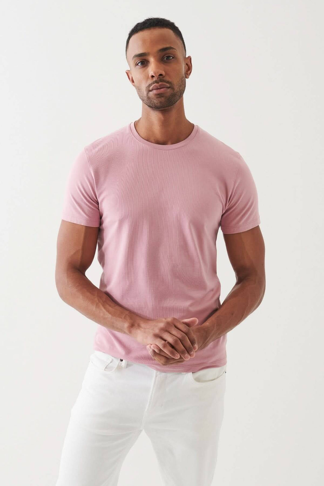 Homme portant un T-shirt en coton Pima rose, style décontracté avec un pantalon blanc, mettant en valeur le confort et l'élégance.