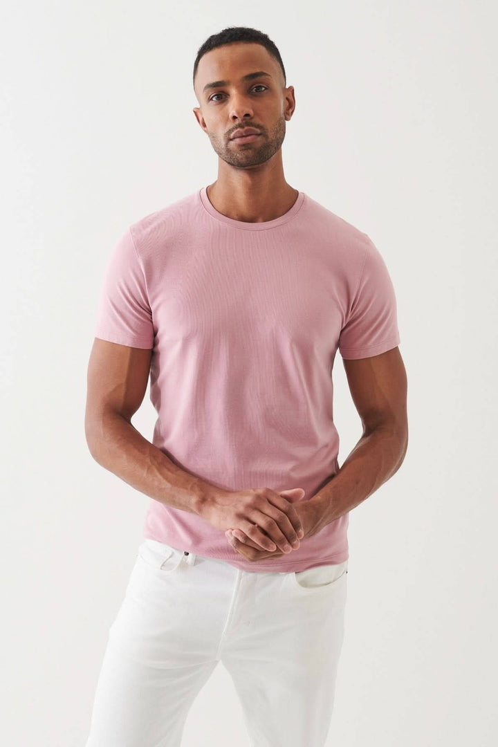 Homme portant un T-shirt en coton Pima rose, style décontracté avec un pantalon blanc, mettant en valeur le confort et l'élégance.