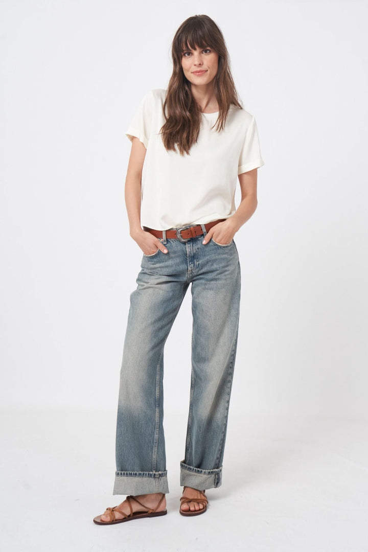 Femme portant un t-shirt blanc et un jean large, avec des sandales et une ceinture, pour un look chic et décontracté.