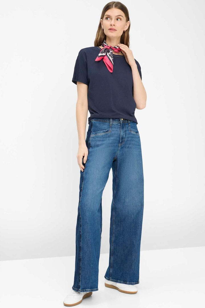 Femme portant le T-shirt encolure perlée Caelen, coupe décontractée, avec jeans évasé et foulard rouge. Look moderne et fluide.