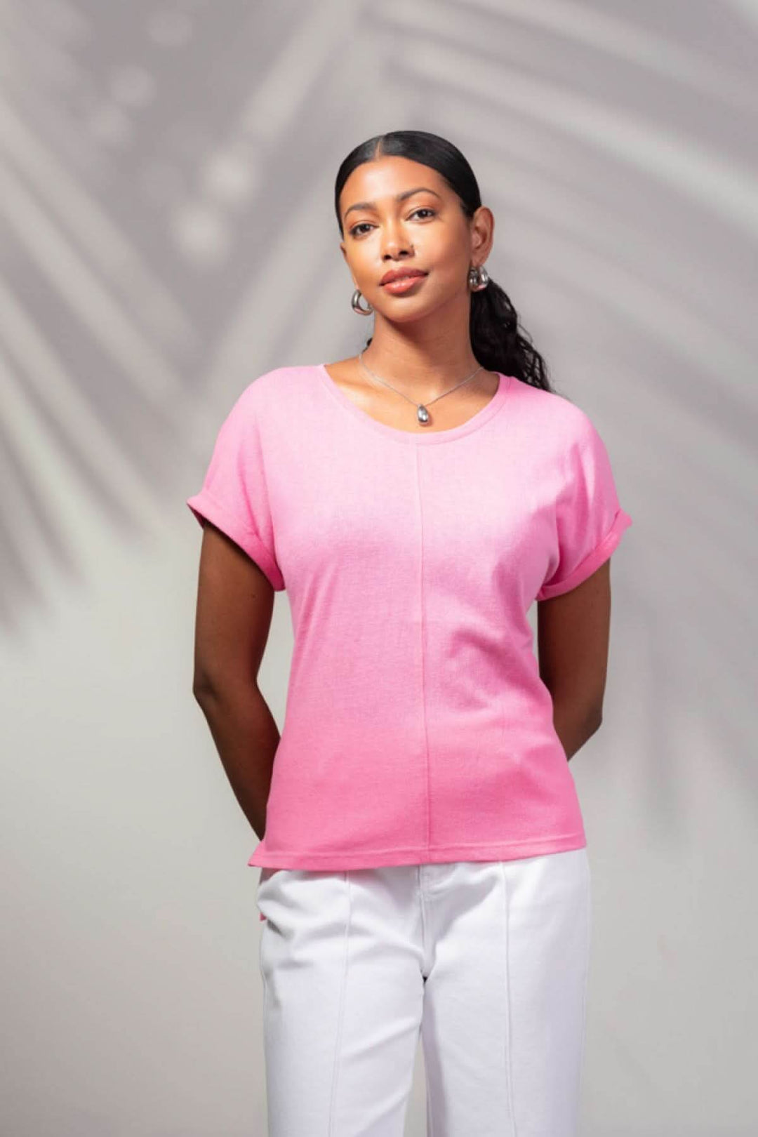 T-shirt à encolure ronde rose porté par une femme, avec couture à l'avant et pantalon blanc, look moderne et décontracté.