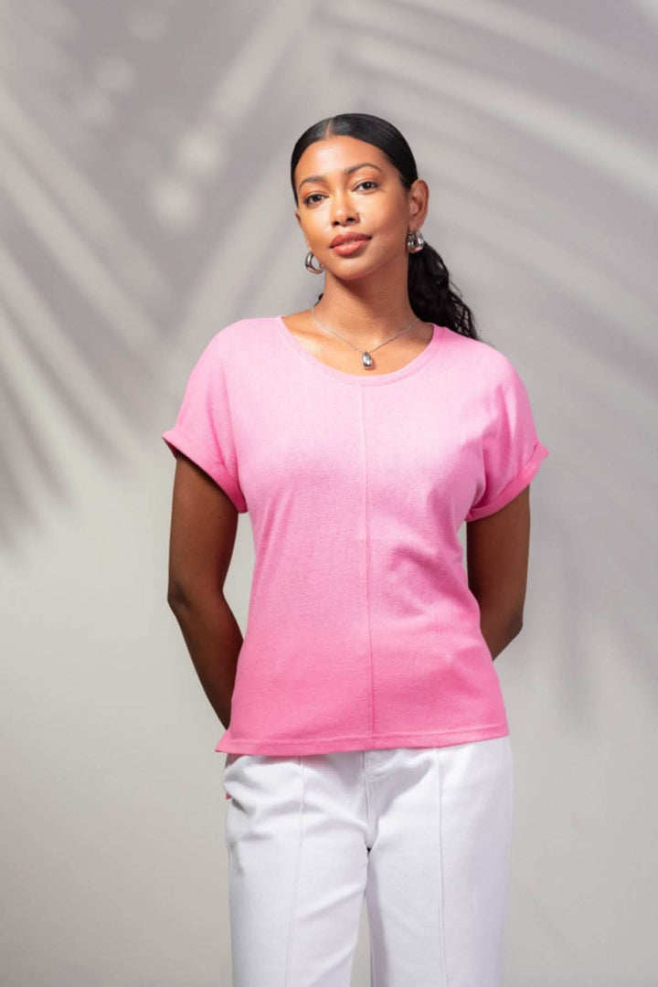 T-shirt à encolure ronde rose porté par une femme, avec couture à l'avant et pantalon blanc, look moderne et décontracté.