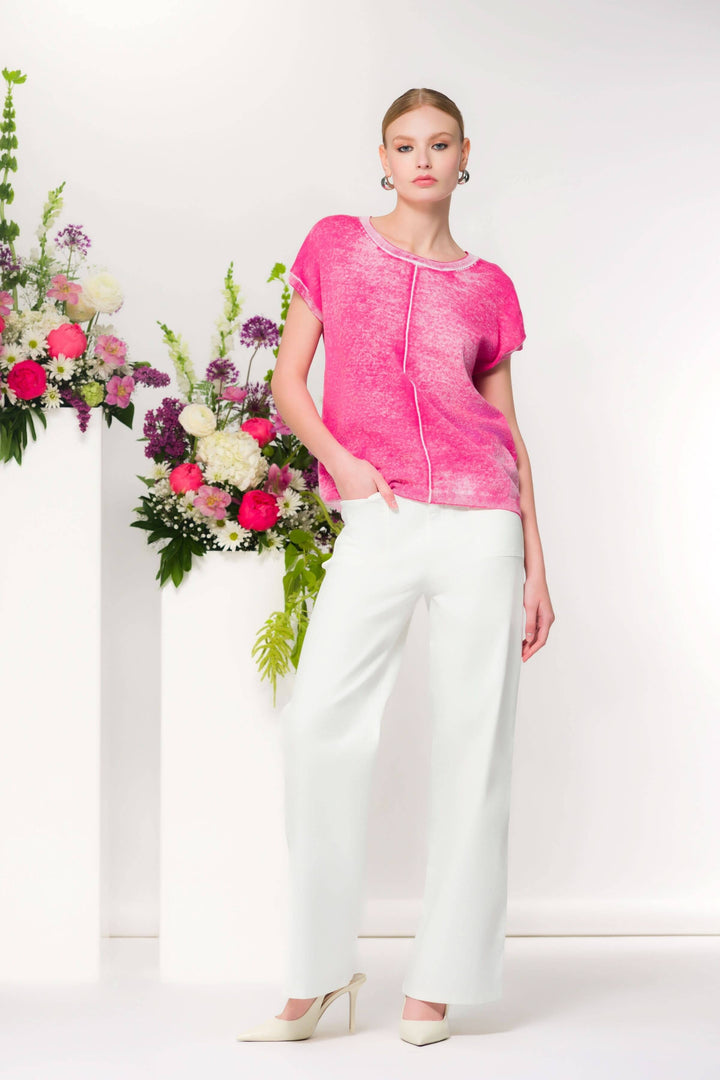 Femme portant un t-shirt fluide rose avec pantalon blanc, devant des fleurs décoratives