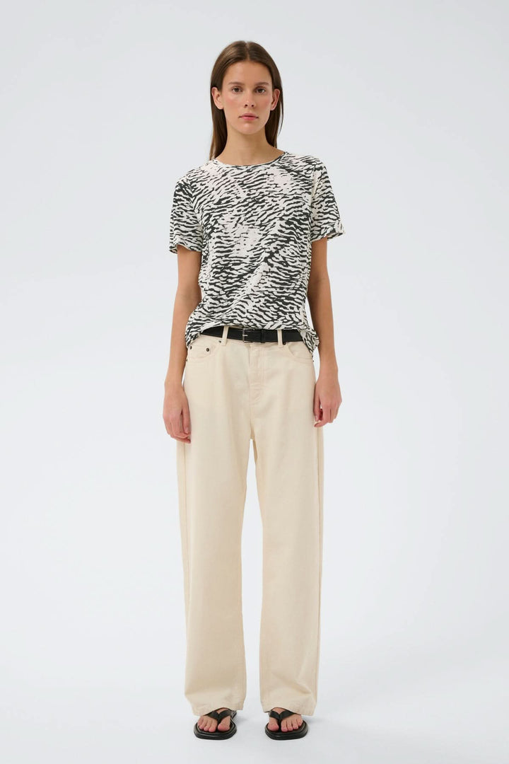 Femme portant un T-shirt imprimé Alma avec coupe droite et imprimé graphique, style décontracté et moderne.