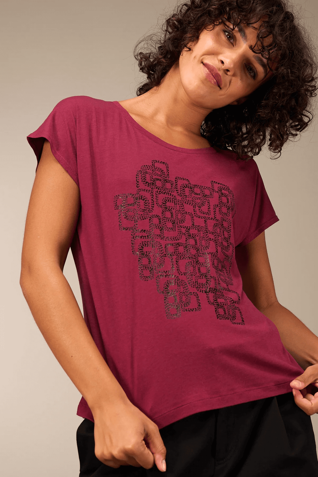 Femme portant un t-shirt imprimé graphique violet avec manches courtes, style décontracté, col rond, idéal pour un look casual chic.