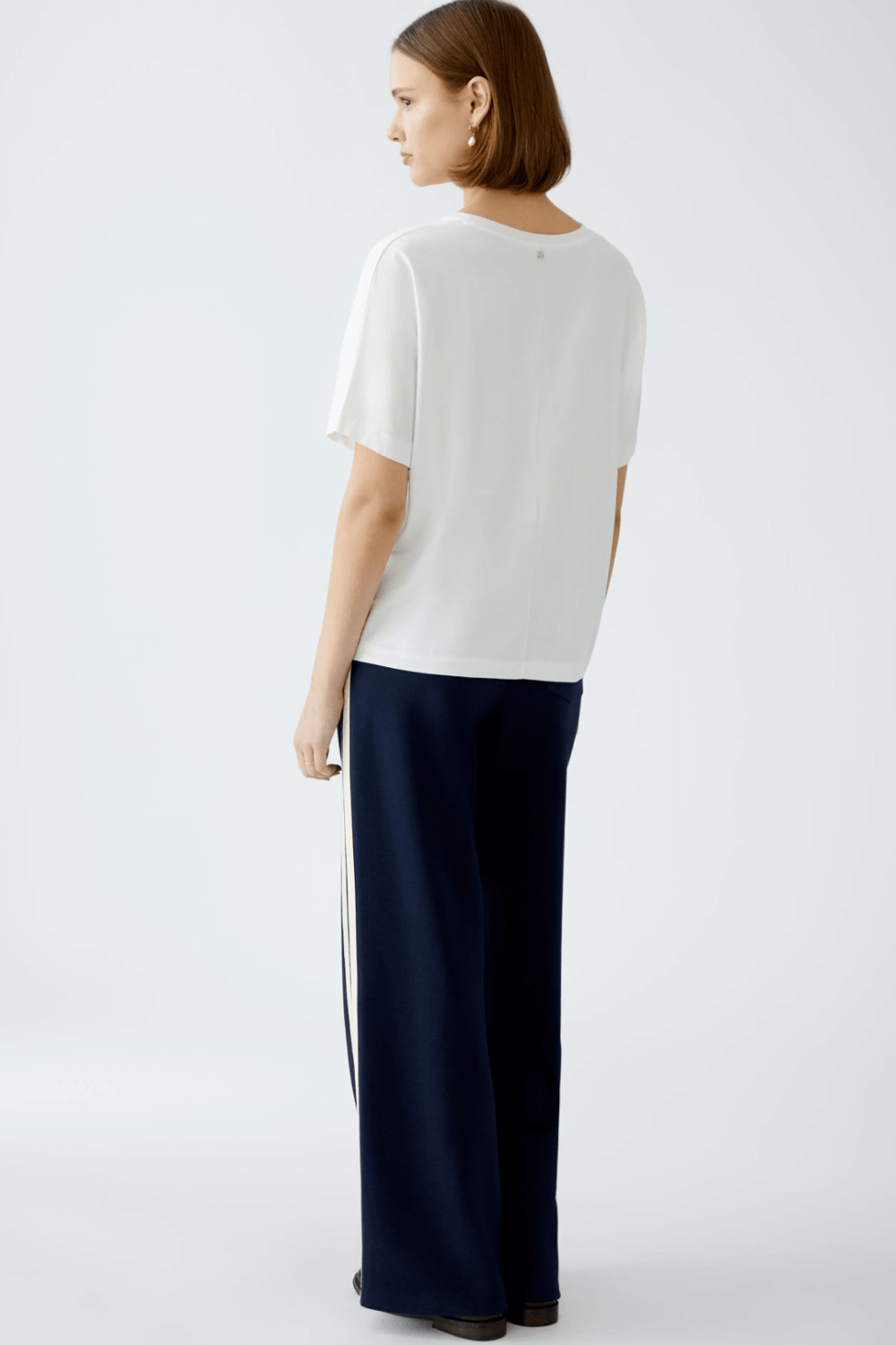 Femme de dos portant un t-shirt blanc et un pantalon de sport, dégageant une allure décontractée et élégante.