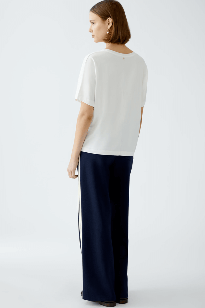 Femme de dos portant un t-shirt blanc et un pantalon de sport, dégageant une allure décontractée et élégante.