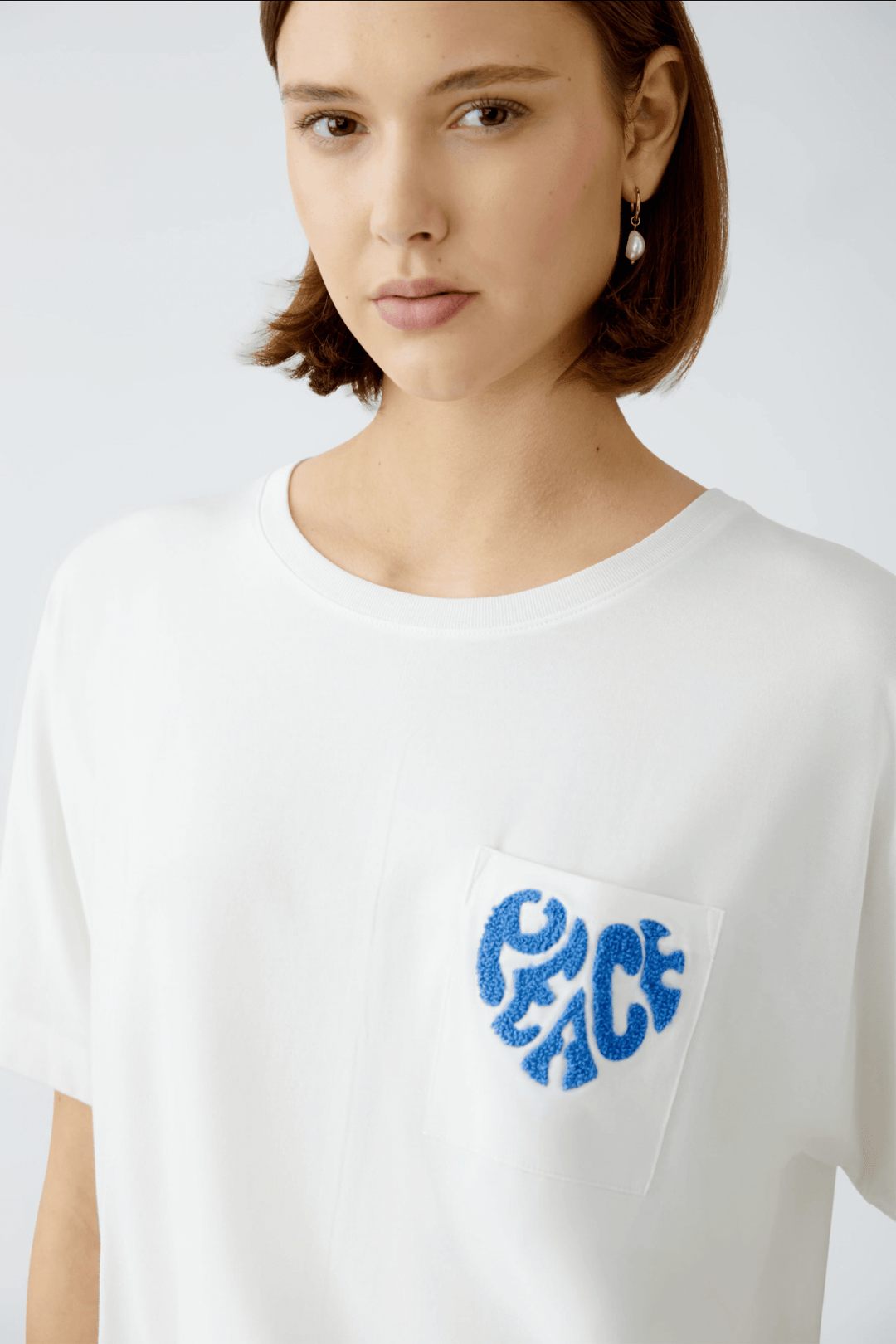 T-shirt blanc avec broderie bleue "Peace" sur la poche, style décontracté et élégant.