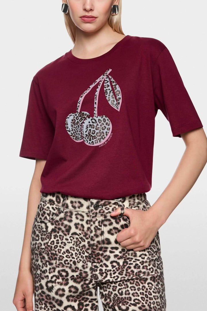 Femme portant un T-shirt imprimé cerises léopard, manches courtes, en coton bio, design décontracté et responsable.
