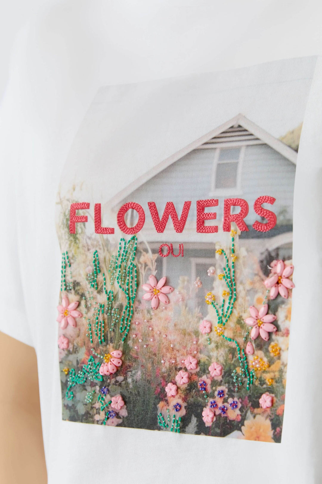 T-shirt imprimé graphique avec motif floral coloré et maison en arrière-plan, "FLOWERS OUI" écrit. Mode moderne et artistique.