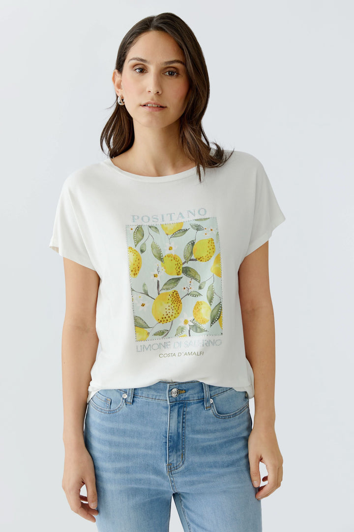 Femme portant un T-shirt imprimé à manches courtes avec un motif graphique de citrons, style décontracté et moderne, encolure ronde.