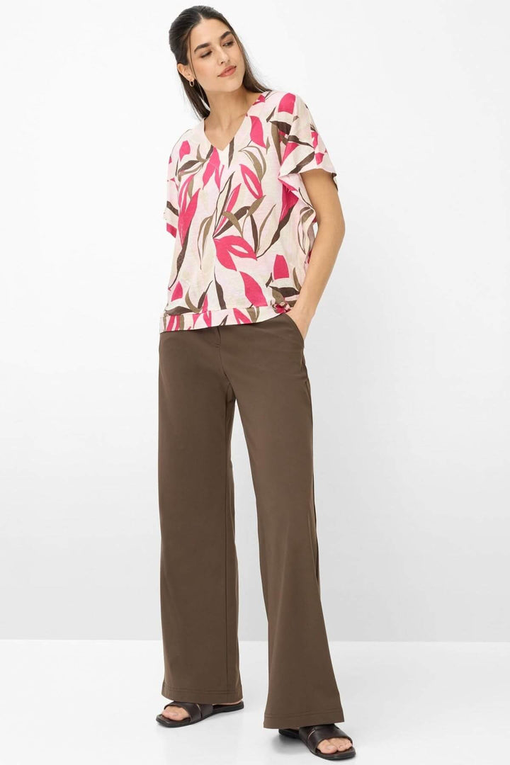 Femme portant le T-shirt imprimé végétal Cassie, coupe ample et encolure en V, avec un pantalon marron; style décontracté et moderne.