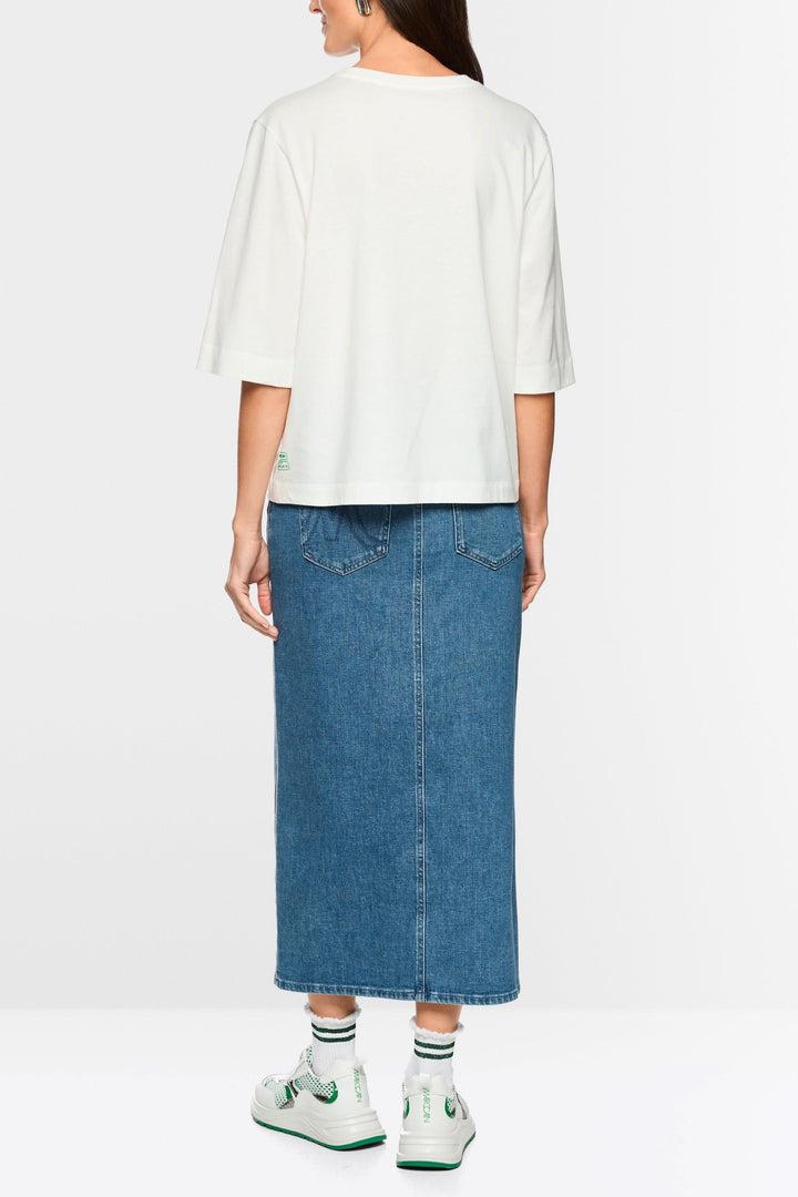 Dos d'une personne portant un T-shirt imprimée matcha « Rethink Together » avec une jupe en denim et des baskets blanches.