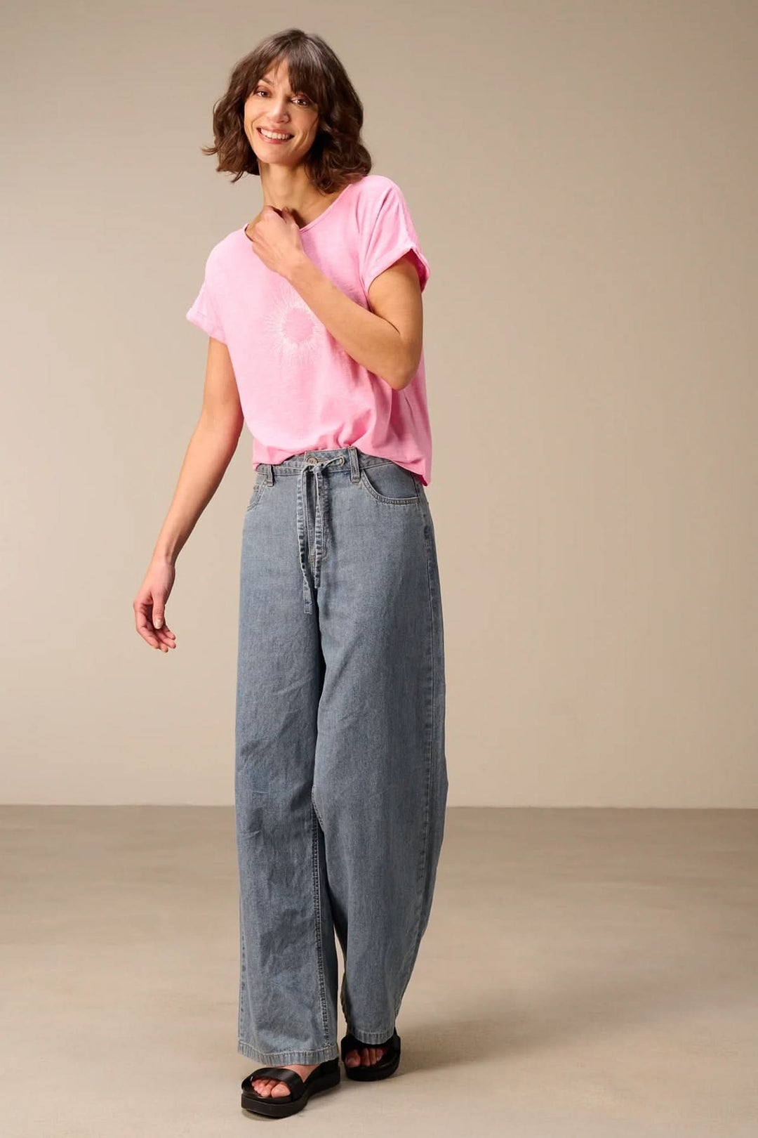 Femme portant un T-shirt à manches courtes coupe décontractée rose et pantalon ample, style casual et confortable.