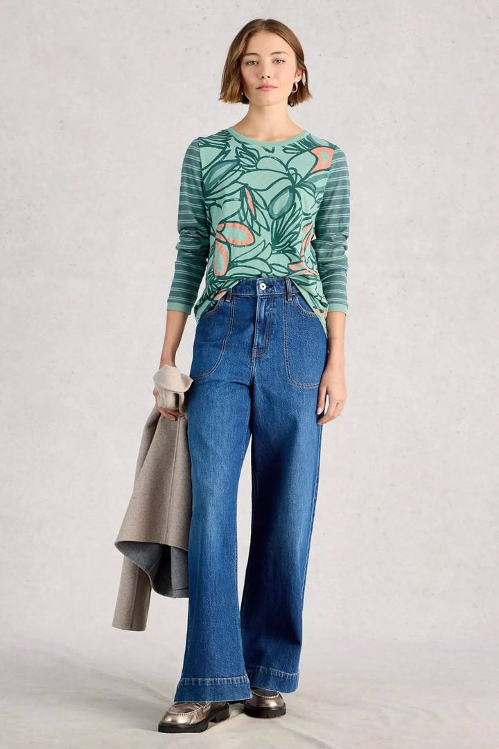 Femme portant un T-shirt à manches longues Clara avec imprimé, associé à un jean large et tenant une veste grise.