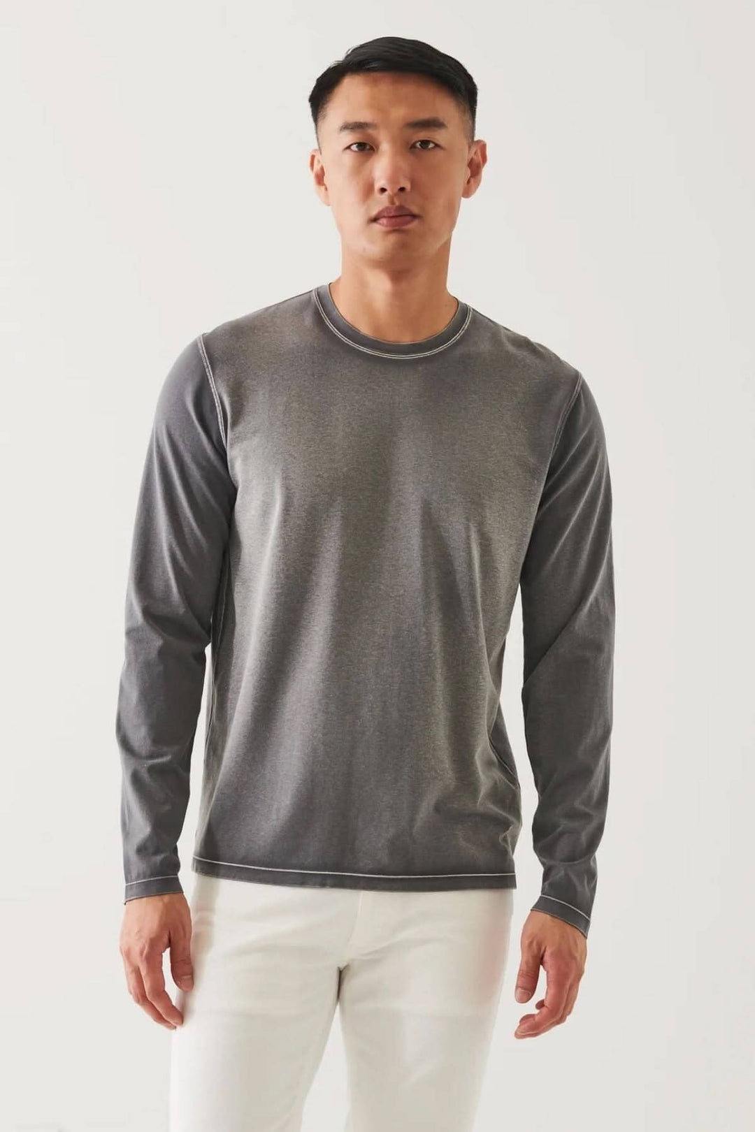 Homme portant un t-shirt à manches longues en coton pima gris avec col rond, style décontracté sur fond blanc.
