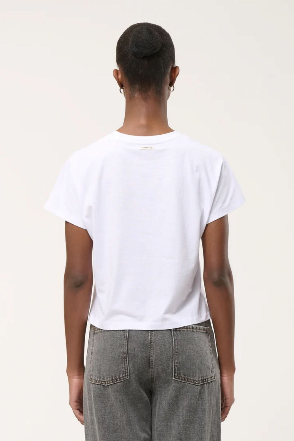 Vue arrière du T-shirt à ourlet asymétrique blanc porté, montrant la coupe droite et l'ourlet subtil sur un modèle en jean gris.