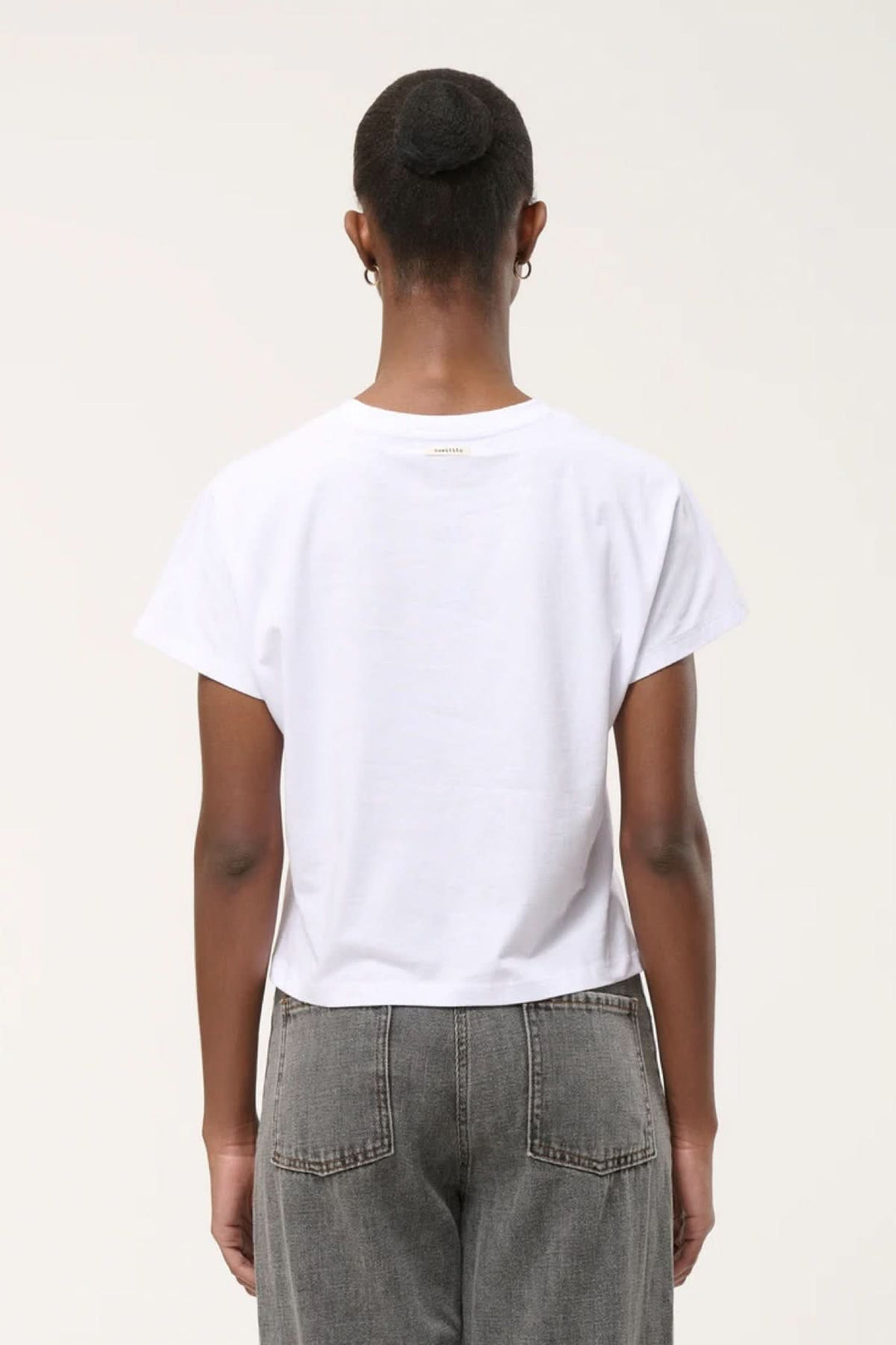 Vue arrière du T-shirt à ourlet asymétrique blanc porté, montrant la coupe droite et l'ourlet subtil sur un modèle en jean gris.