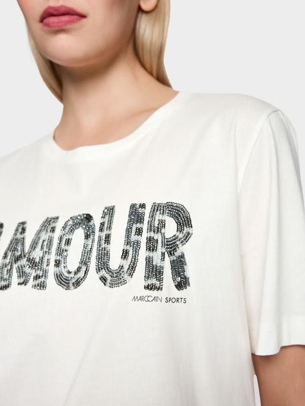 T-shirt à paillettes décontracté avec slogan « Amour », col rond, manches courtes, en coton, porté par mannequin. Parfait pour un look moderne.