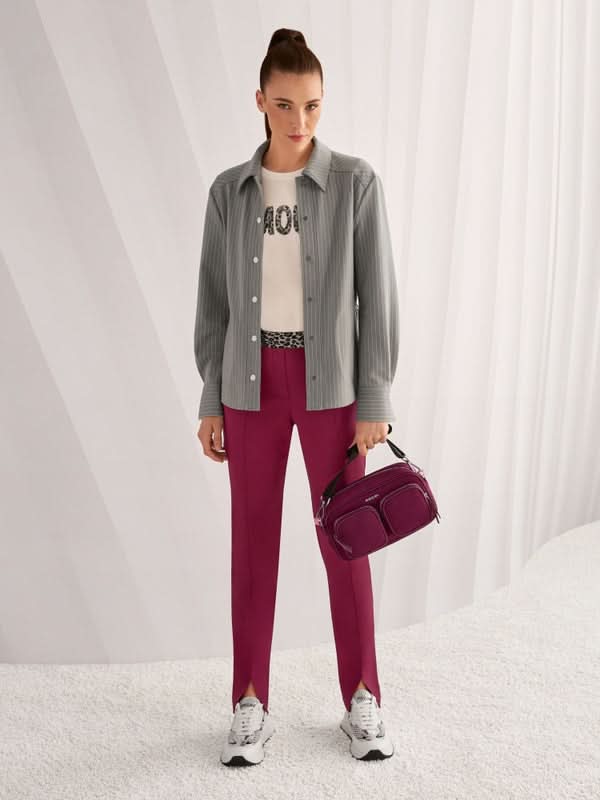Femme portant un T-shirt à paillettes avec une chemise grise ouverte, pantalon rose, et un sac violet, style moderne et décontracté.